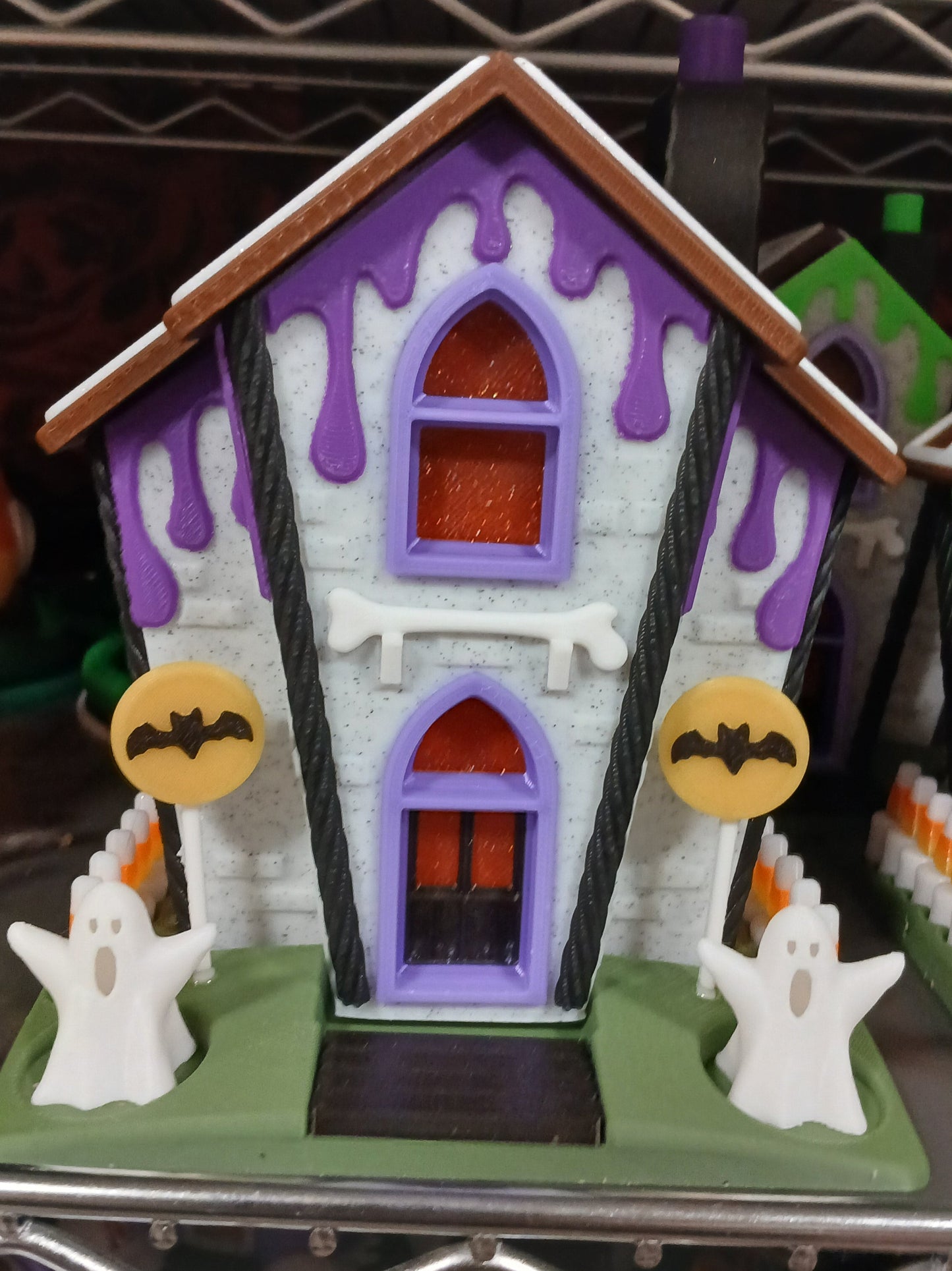 Halloween-themed toy house with purple roof, green base, and decorative elements on a metal rack.